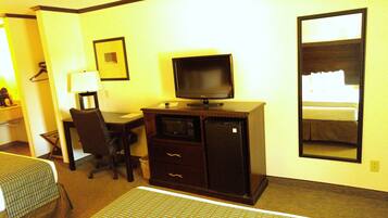 Habitación de hotel con escritorio, silla, televisor y un espejo grande.