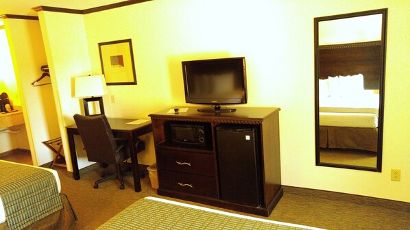 Habitación de hotel con escritorio, silla, televisor y un espejo grande.