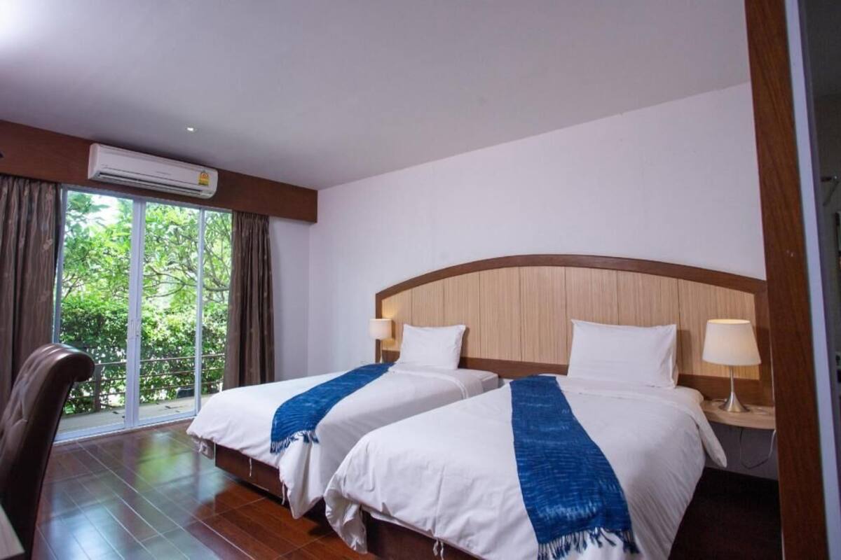 Een hotelkamer met twee bedden, een groot raam met gordijnen, een airconditioner en een houten hoofdeinde.
