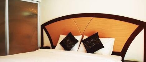 Una cama bien hecha con cabecera de madera y dos almohadas decorativas.