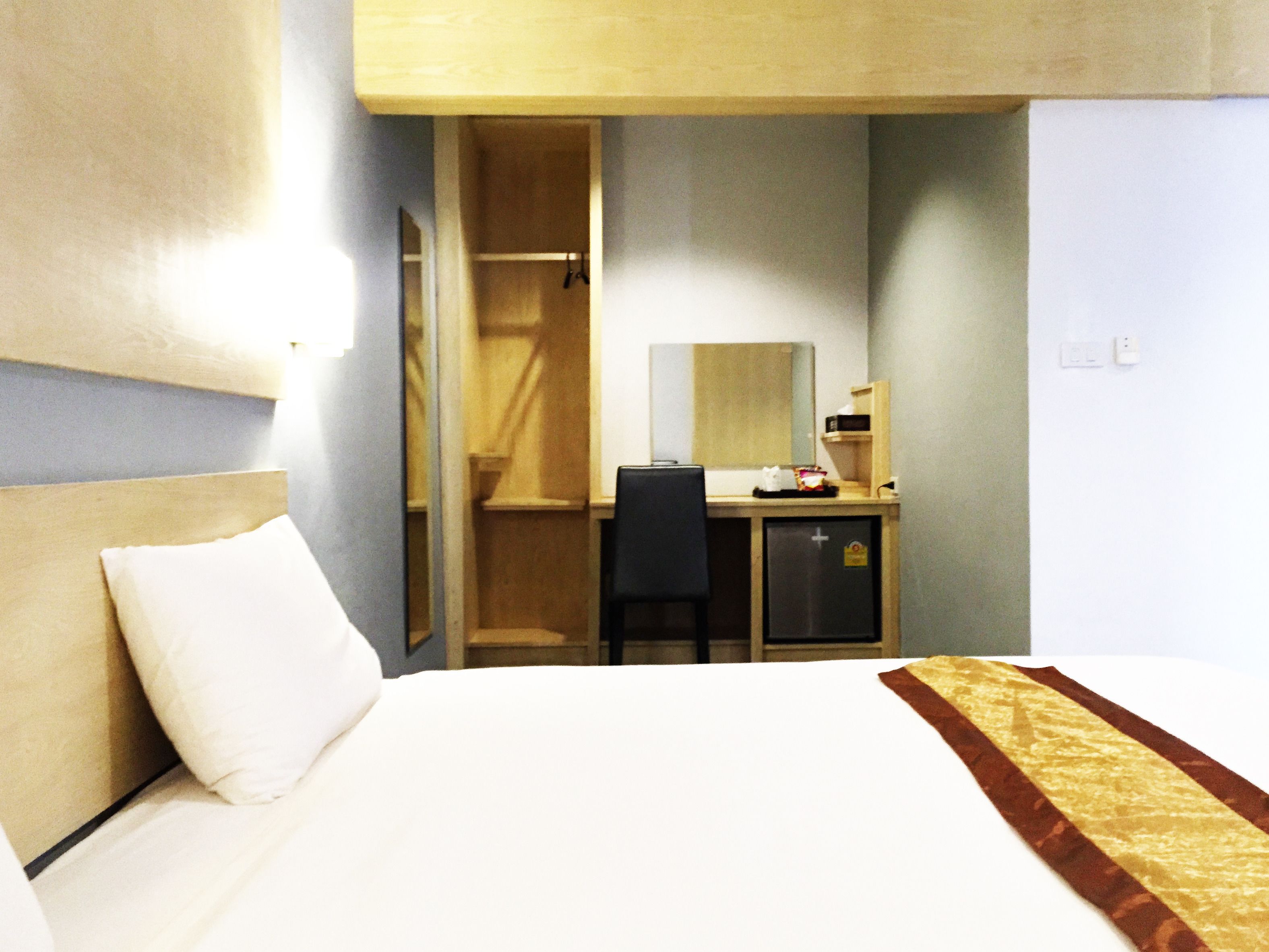 A hotel room with a bed, a desk, a chair, a wardrobe, and a mirror.