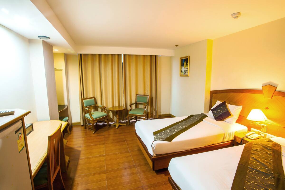 Een hotelkamer met twee bedden, een bureau, een stoel, een tafeltje en een lamp.