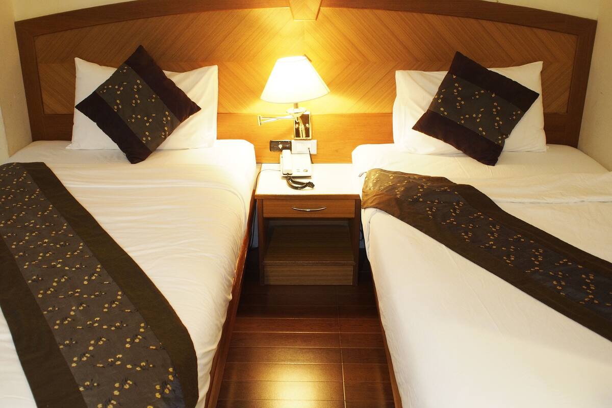 Een hotelkamer met twee bedden, een nachtkastje met een lamp en een telefoon.