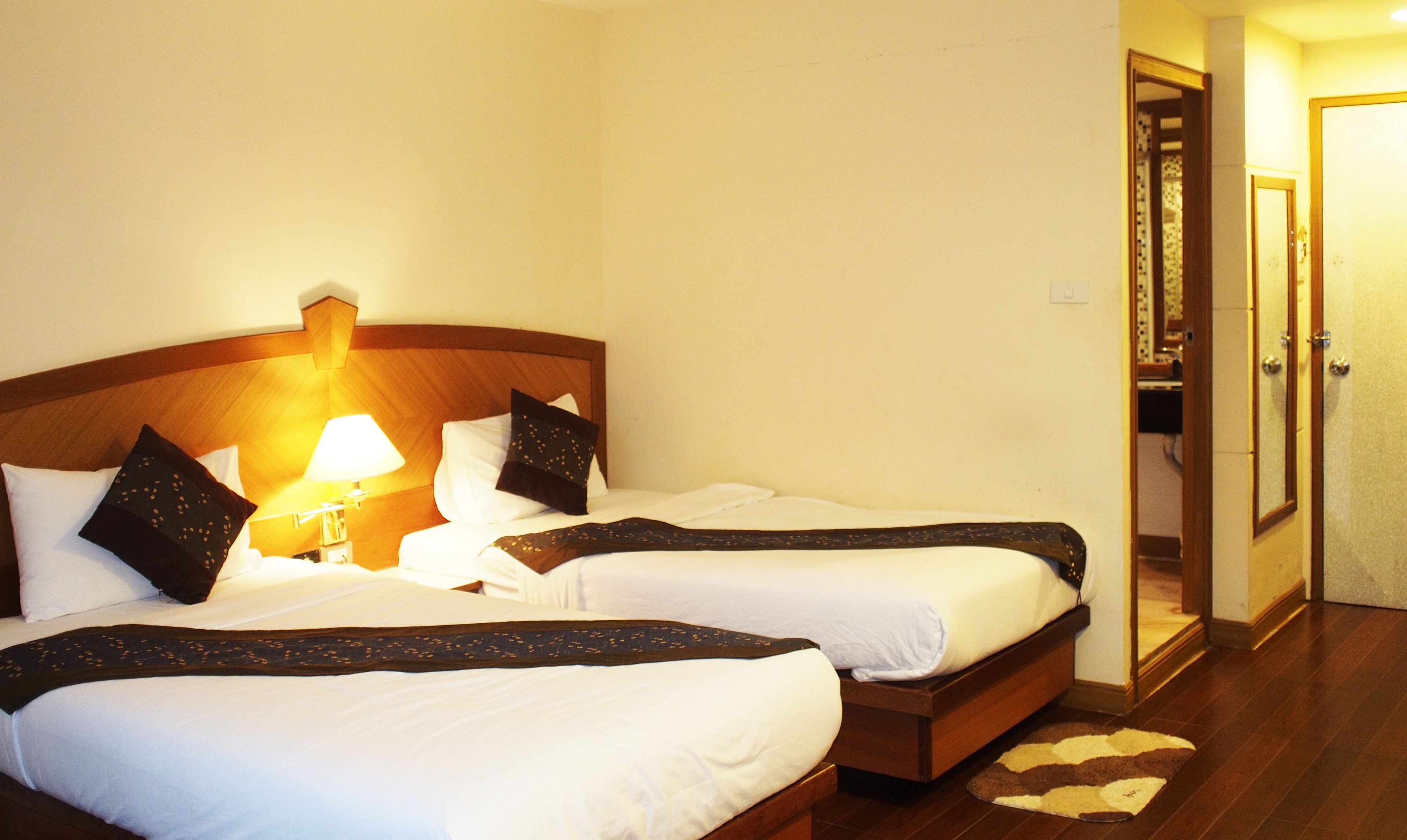 Een hotelkamer met twee enkele bedden, een nachtkastje met een lamp en een houten hoofdeinde.