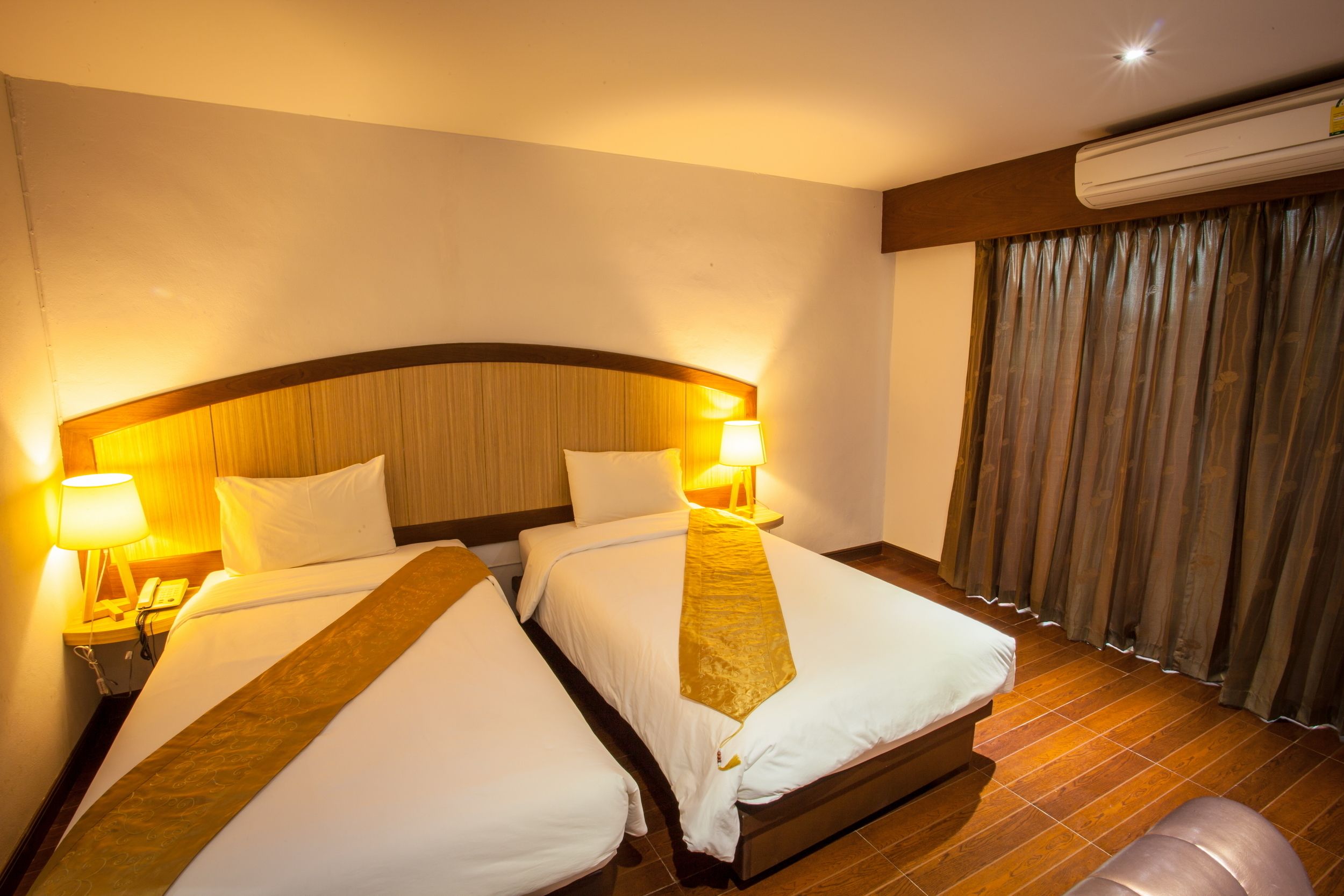 A hotel room with two beds, a wooden headboard, a nightstand with a lamp, and an air conditioning unit.