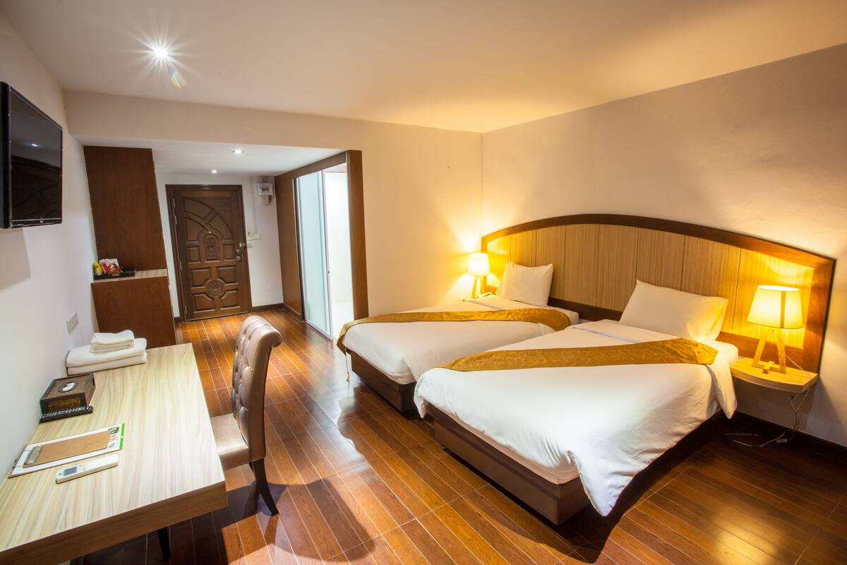 Een hotelkamer met twee bedden, een houten bureau, een stoel, een televisie en een deur naar een andere kamer.