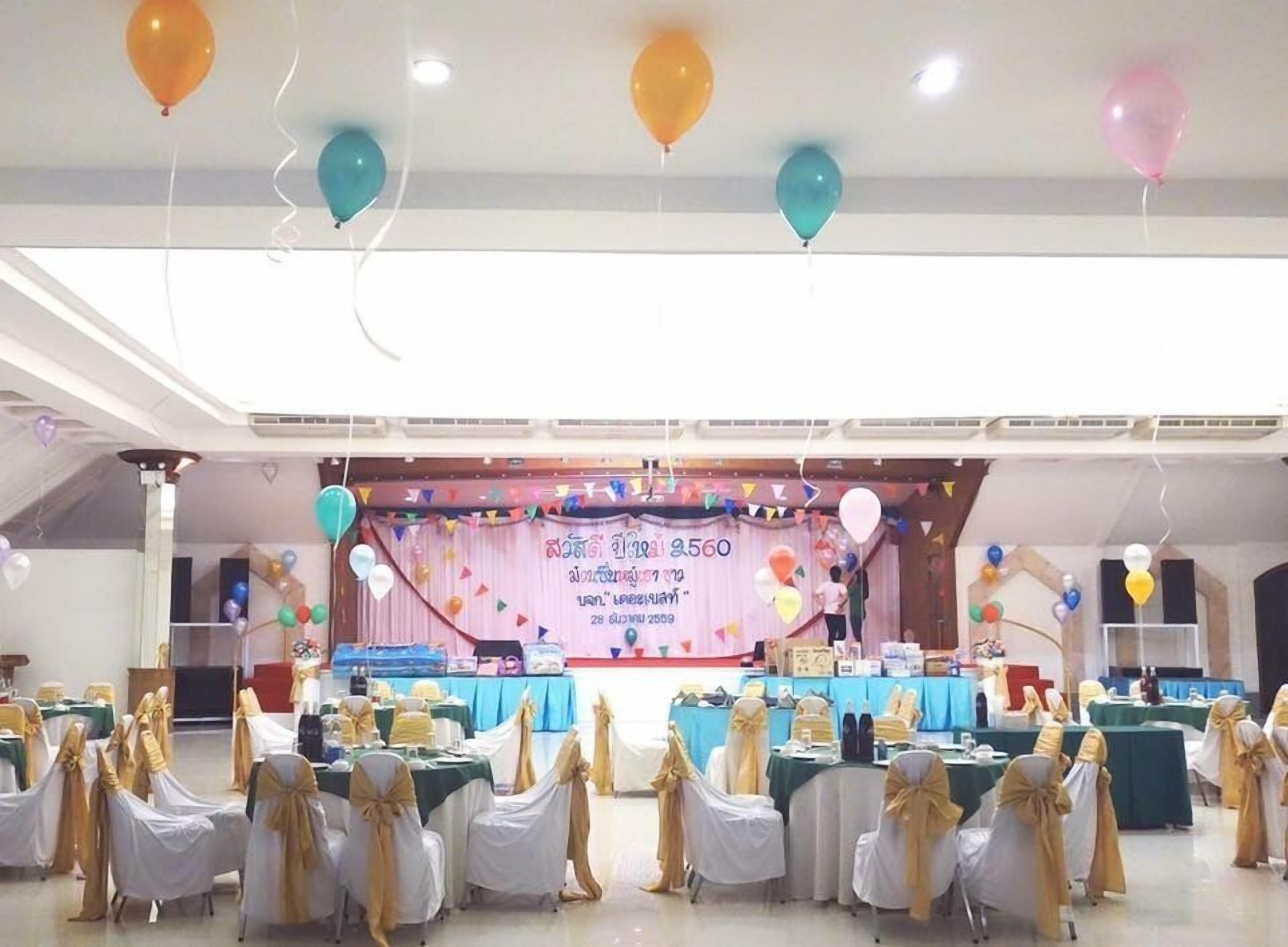 A banquet hall with tables set for an event, decorated with balloons and draped with white and gold sashes.