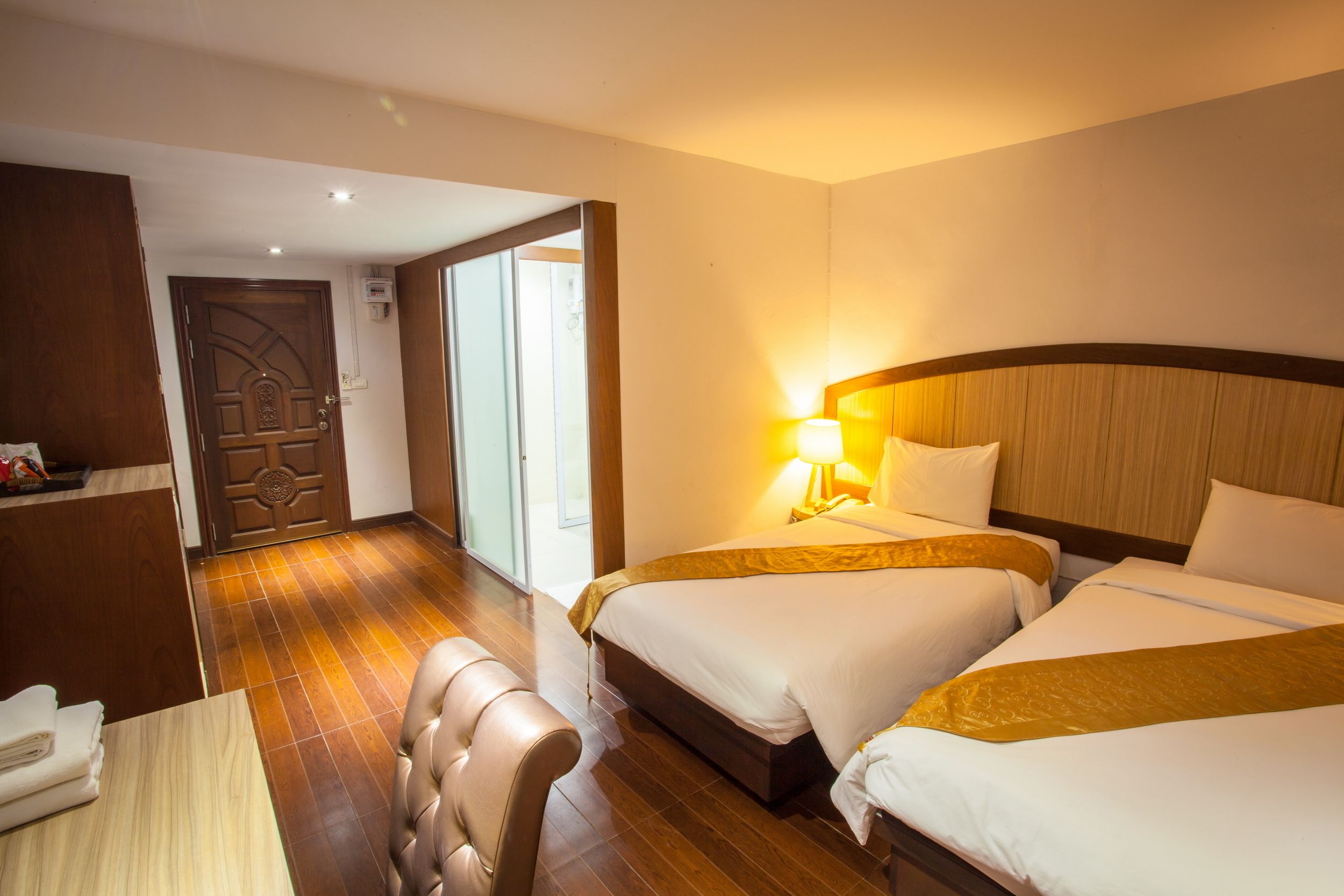 A hotel room with two beds, a wooden desk, a chair, and a door leading to a balcony.