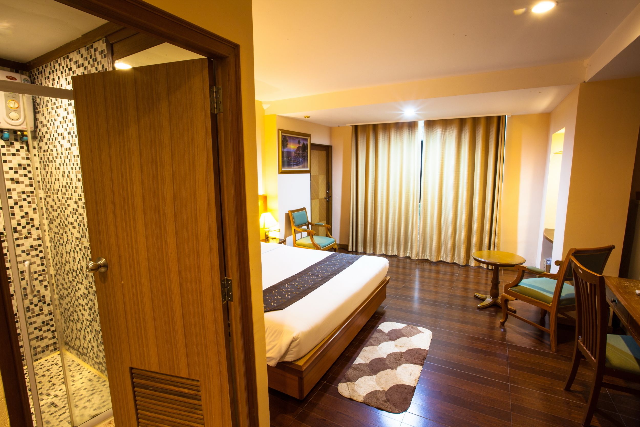 Camera d'albergo con un letto grande, una porta in legno, un angolo doccia, un tavolino e una sedia.