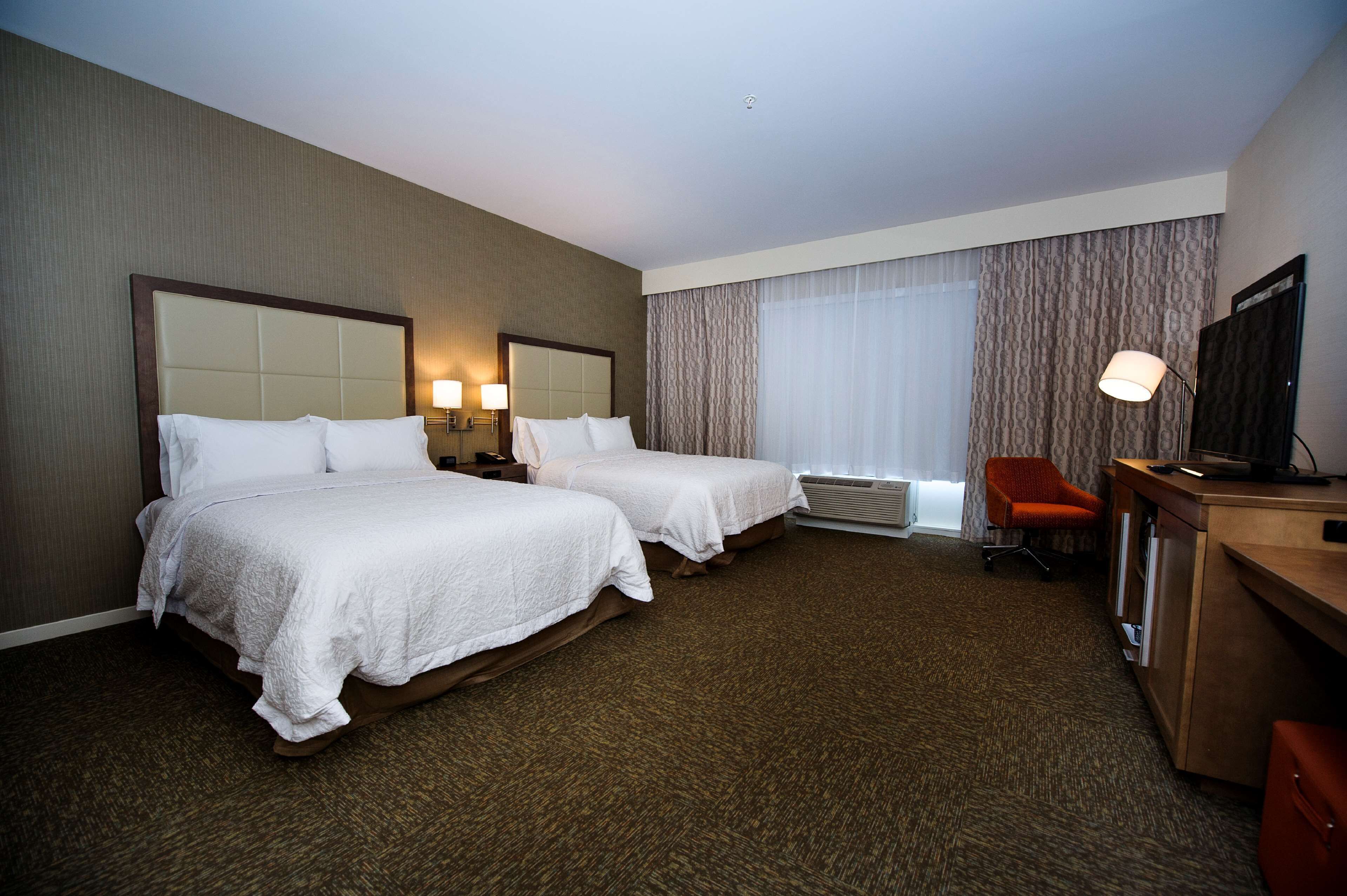 A hotel room with two beds, a desk, a chair, and a television.