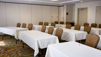 Une salle de conférence dotée de plusieurs tables et de nombreuses chaises, disposées en rangées.