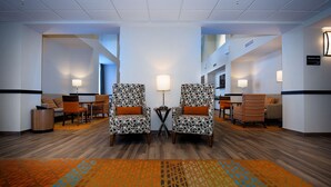 A hotel lobby with two patterned armchairs, a small table, and a carpeted floor. - Hampton Inn & Suites by Hilton Truro (Millbrook First Nation Reserve)
