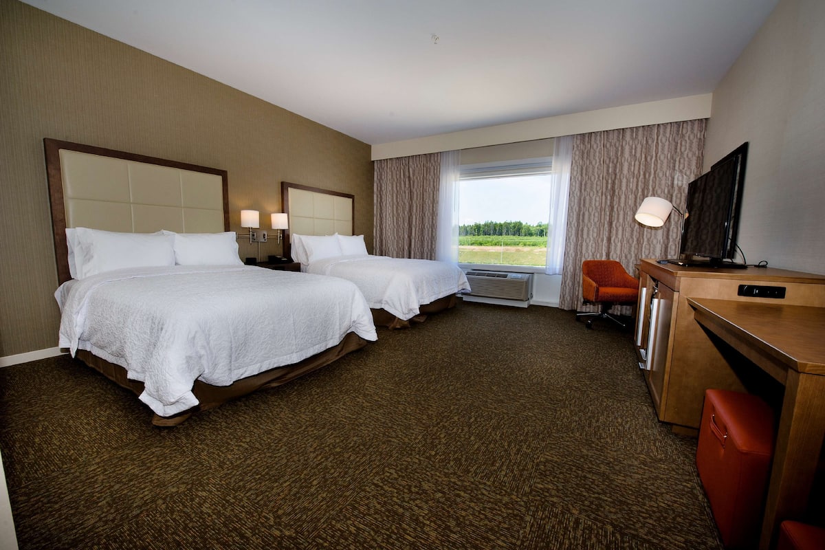 A hotel room with two beds, a desk, a TV, and a view of the outdoors.