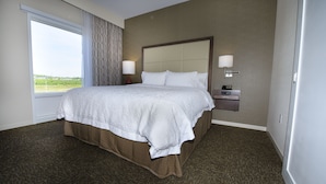 A hotel room with a large bed, two bedside tables with lamps, a view of the outdoors through a window, and a carpeted floor. - Hampton Inn & Suites by Hilton Truro (Millbrook First Nation Reserve)