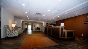 A hotel lobby with a reception desk, patterned chairs, a wooden reception area, and a carpeted floor. - Hampton Inn & Suites by Hilton Truro (Millbrook First Nation Reserve)
