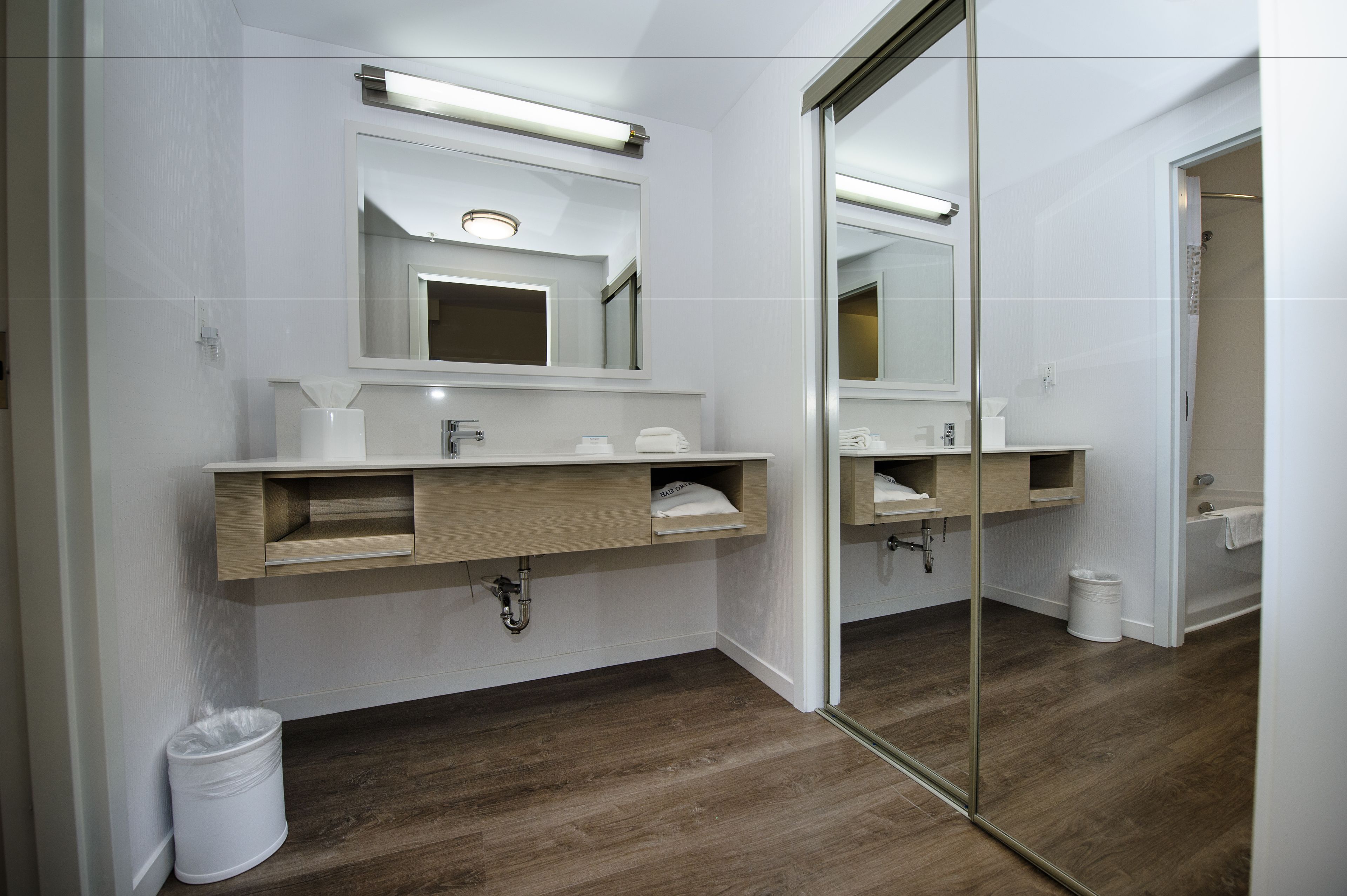 Een moderne badkamer met een grote spiegel, een houten wastafelmeubel en een aparte douchehoek.