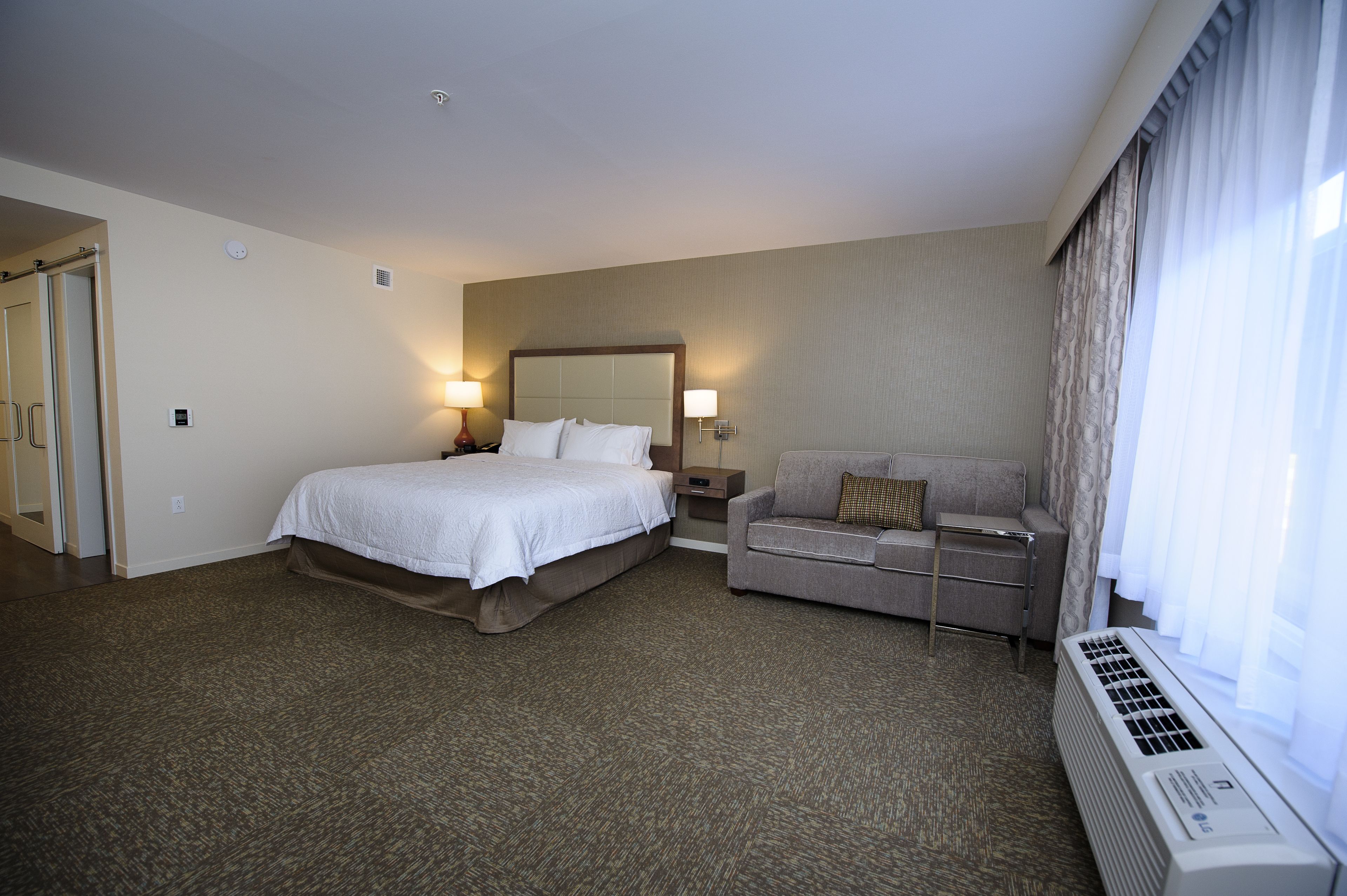 Quarto de hotel com uma cama grande, um sofá, um espelho e uma janela com cortinas.