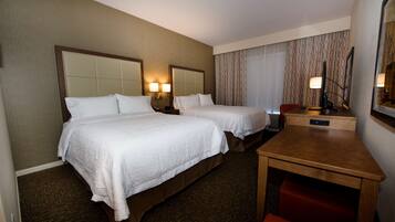 A hotel room with two beds, a desk, and a chair.