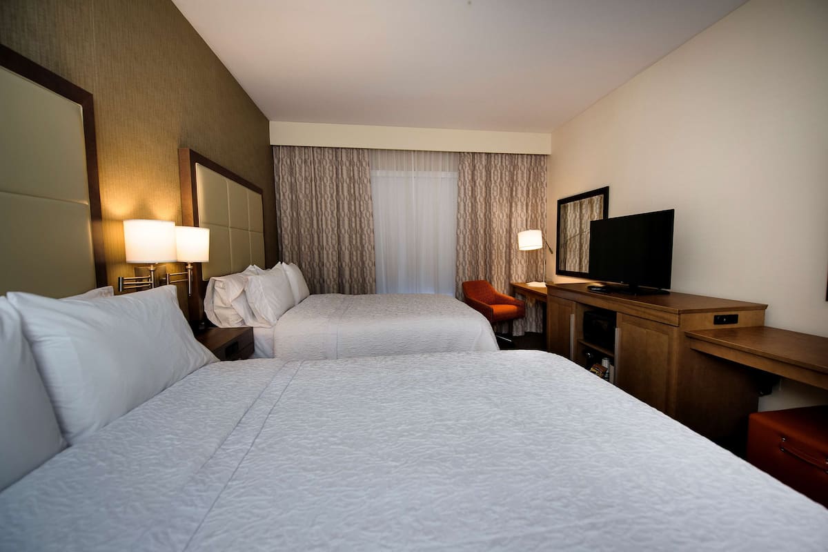 A hotel room with two beds, a desk with a television, and a chair.