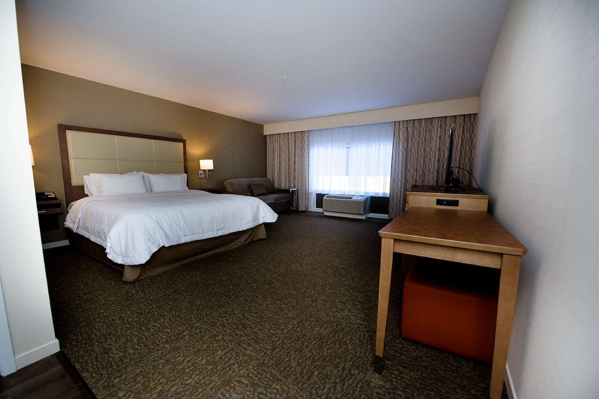 A hotel room with a large bed, a desk, a chair, a nightstand, and a window with curtains.
