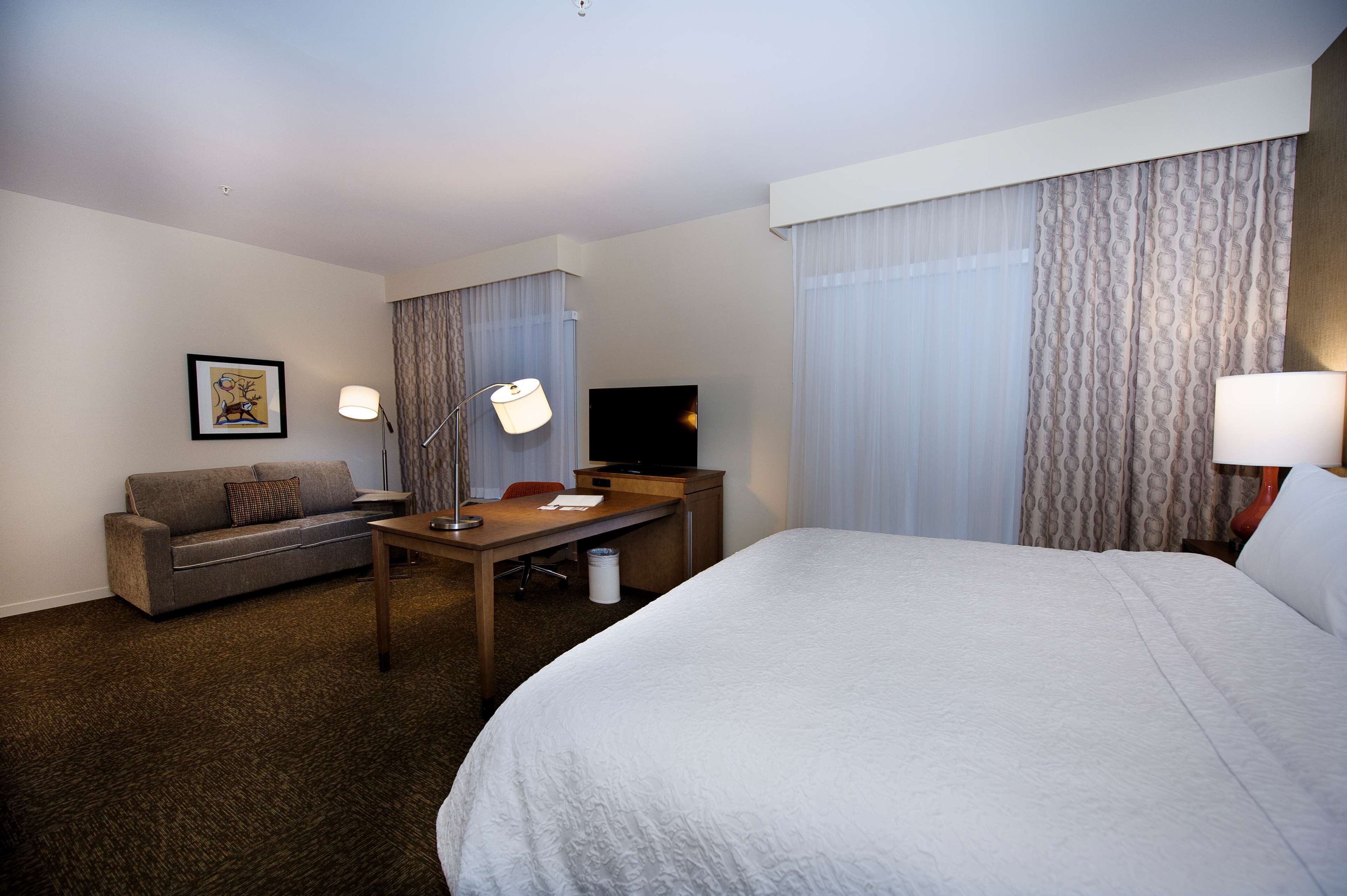 Habitación de hotel con una cama grande, un escritorio, una silla, un sofá, un televisor y cortinas.