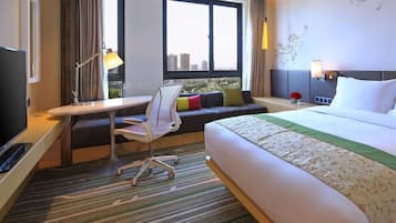 A hotel room with a bed, a desk with a chair, a sofa, a TV, and a window with curtains.