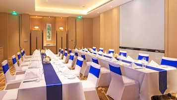 A conference room with multiple tables set for a meeting, equipped with chairs, tables, and a projector screen.