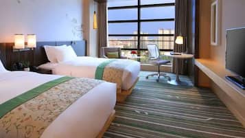 Une chambre d’hôtel avec deux lits, un bureau, une chaise, une télévision et une grande fenêtre donnant sur la ville.