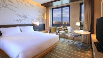 A hotel room with a large bed, a desk with a chair, a television, and a window with a city view.