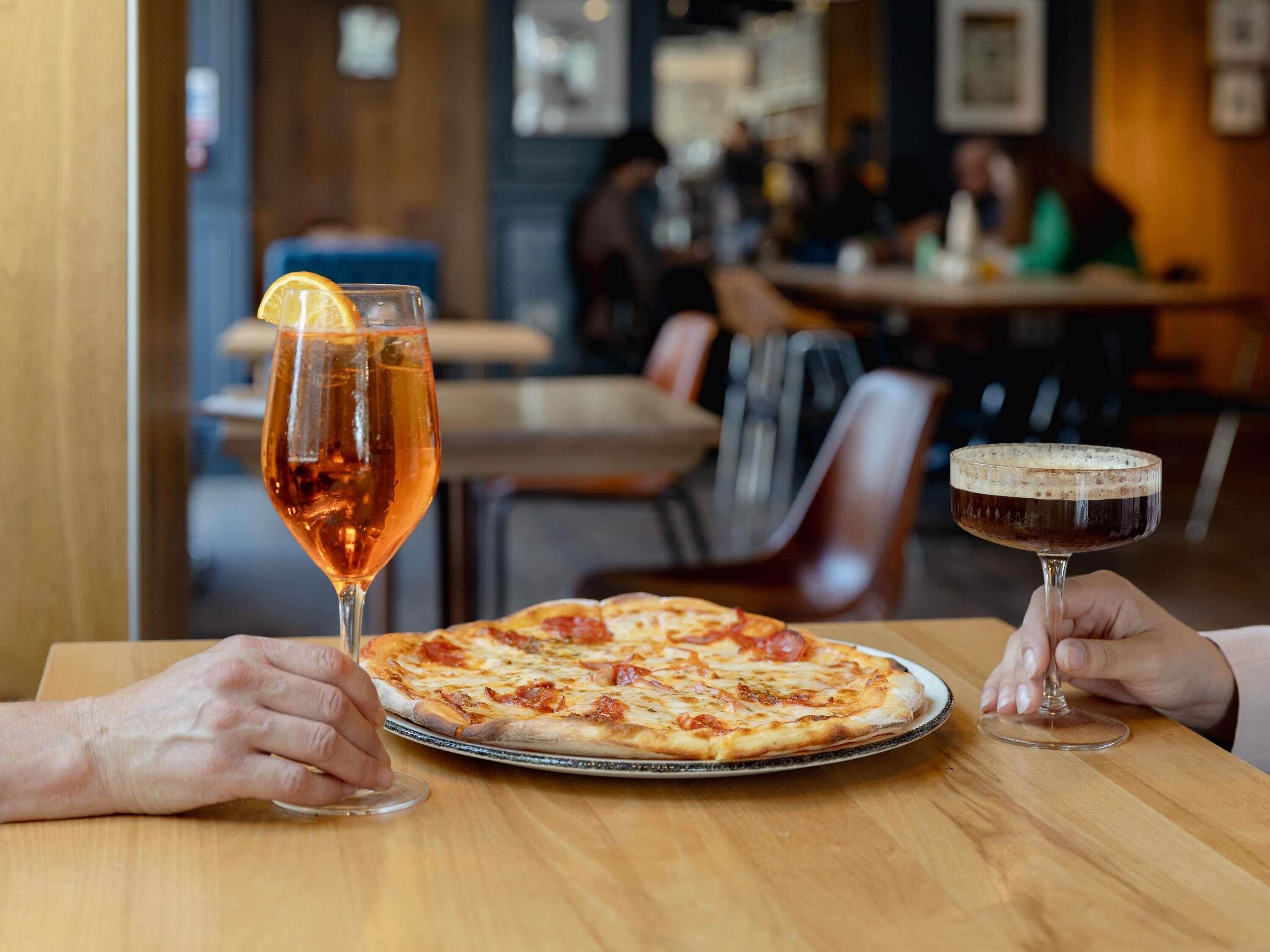 L’intérieur d’un restaurant, avec une pizza sur une table, un verre de vin et un cocktail.