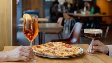 A restaurant interior with a pizza on a table, a glass of wine, and a cocktail.