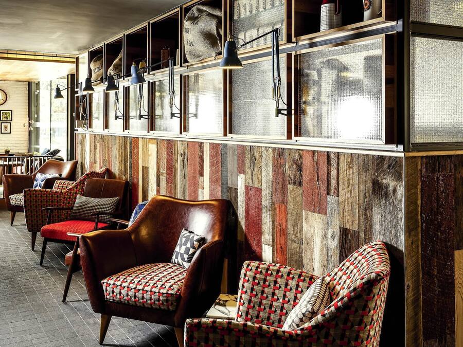 A cozy seating area with leather armchairs and patterned cushions, a wooden wall with a rustic appearance, and a shelf with various items.