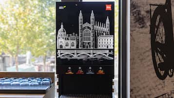 Una cafetera con diseño de paisaje urbano, vista a la ventana y silueta de una bicicleta en la pared.