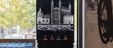 A coffee machine with a cityscape design, a window view, and a bicycle silhouette on the wall.