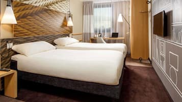 A hotel room with two beds, a desk, a laptop, a TV, and a patterned wall.