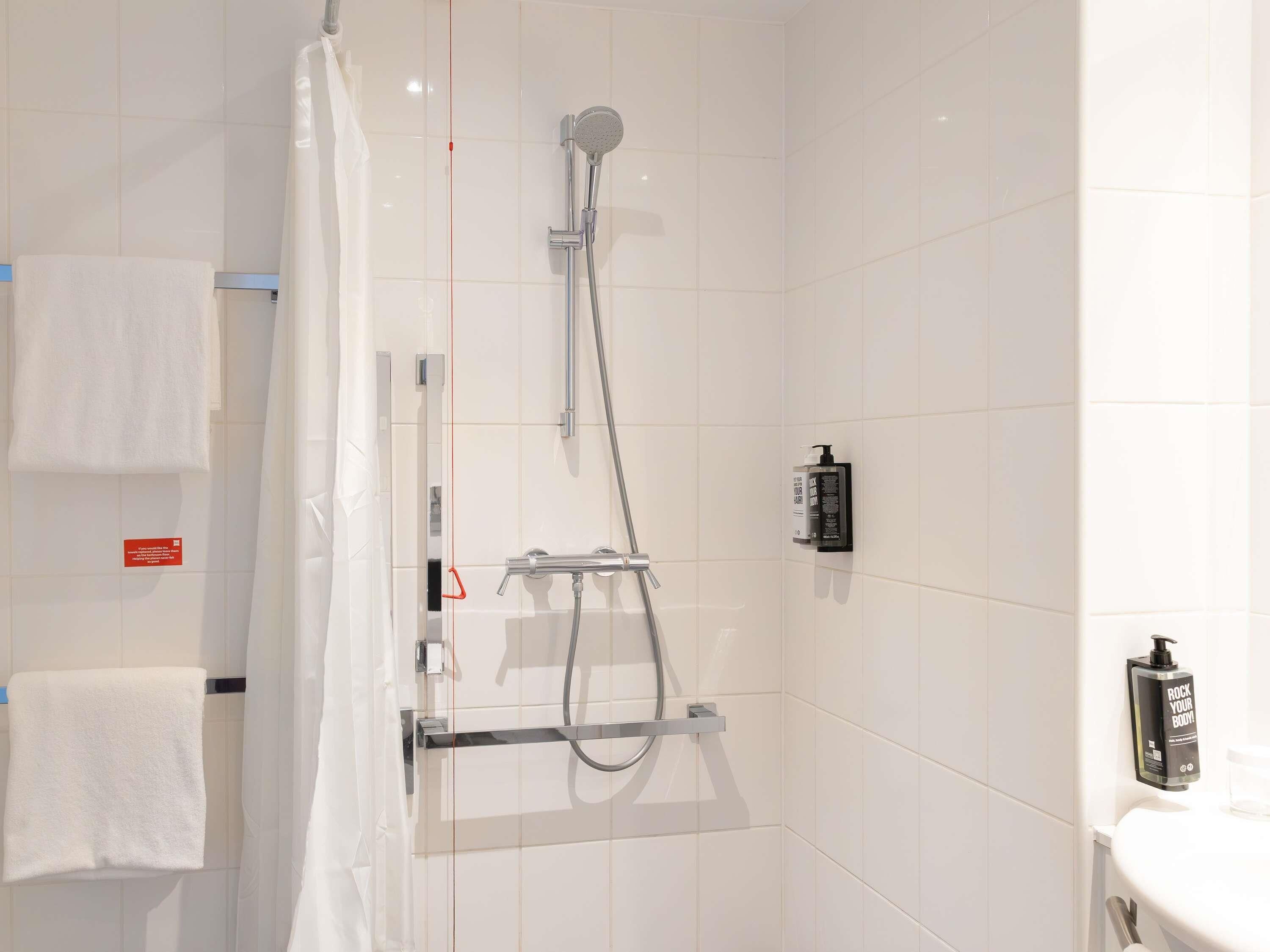 A modern bathroom with a glass shower enclosure, a towel rack, and a soap dispenser.