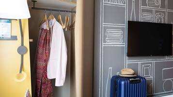 A hotel room with a bed, a wardrobe with clothes, a suitcase, and a wall with a chalkboard design.