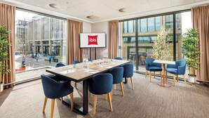 A conference room with a large table, blue chairs, and a screen displaying the ibis logo. - ibis Cambridge Central Station (Cambridge)