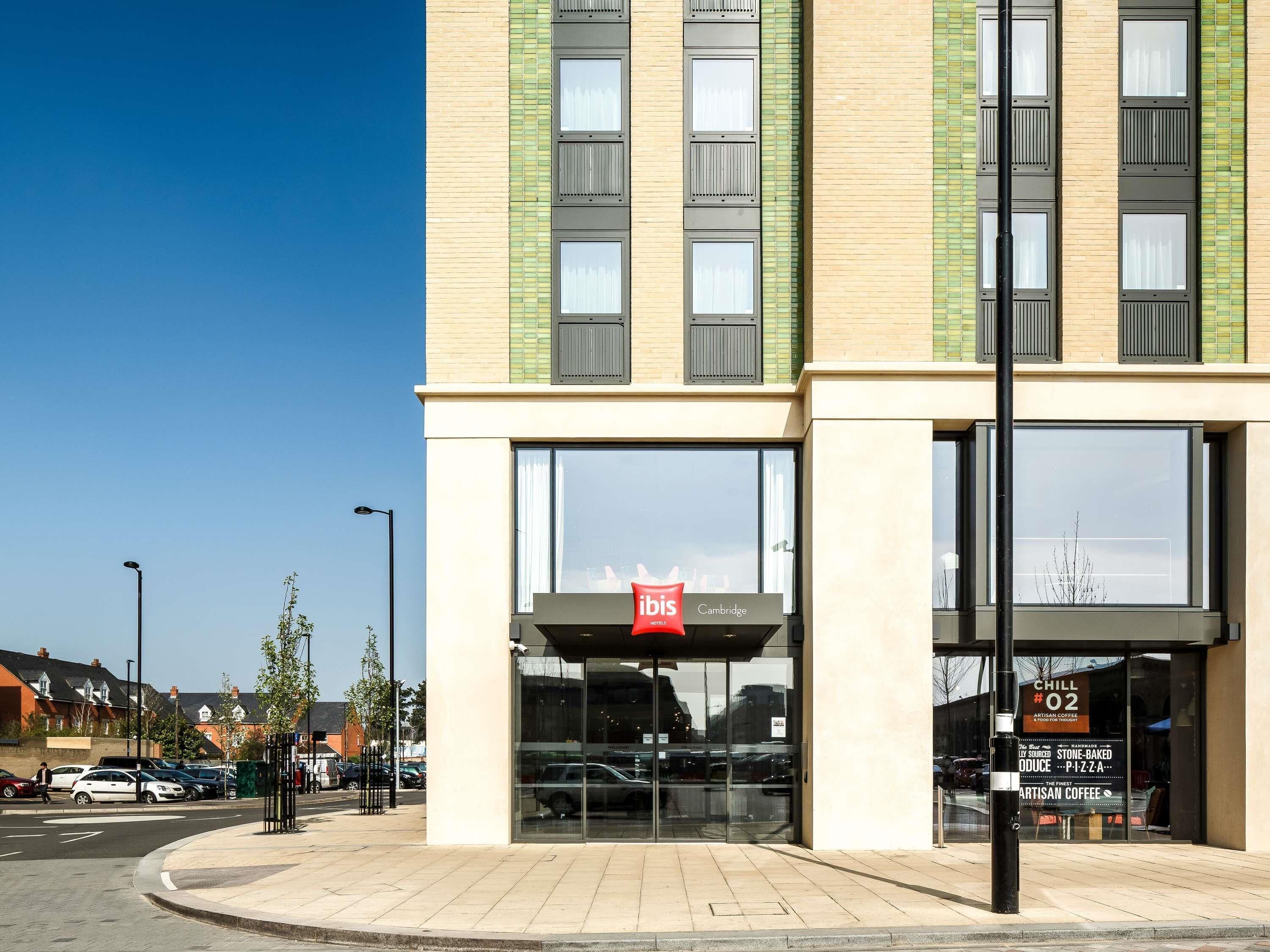 A modern building with a glass entrance, a sign for 'ibis Cambridge Hotel', and a sign for 'CHILL #02' with a menu.