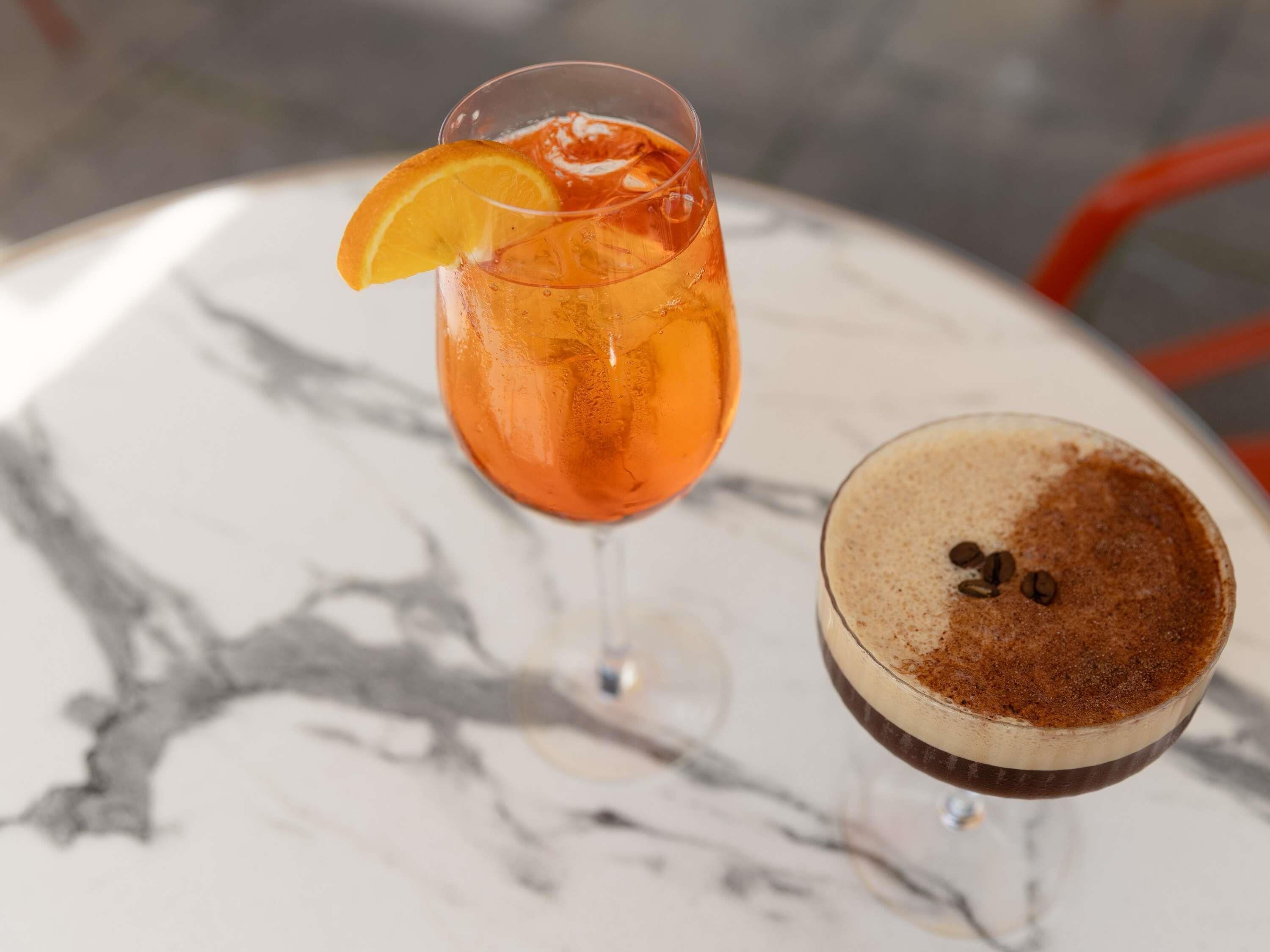 A glass of orange-colored drink with an orange slice garnish on a marble table.