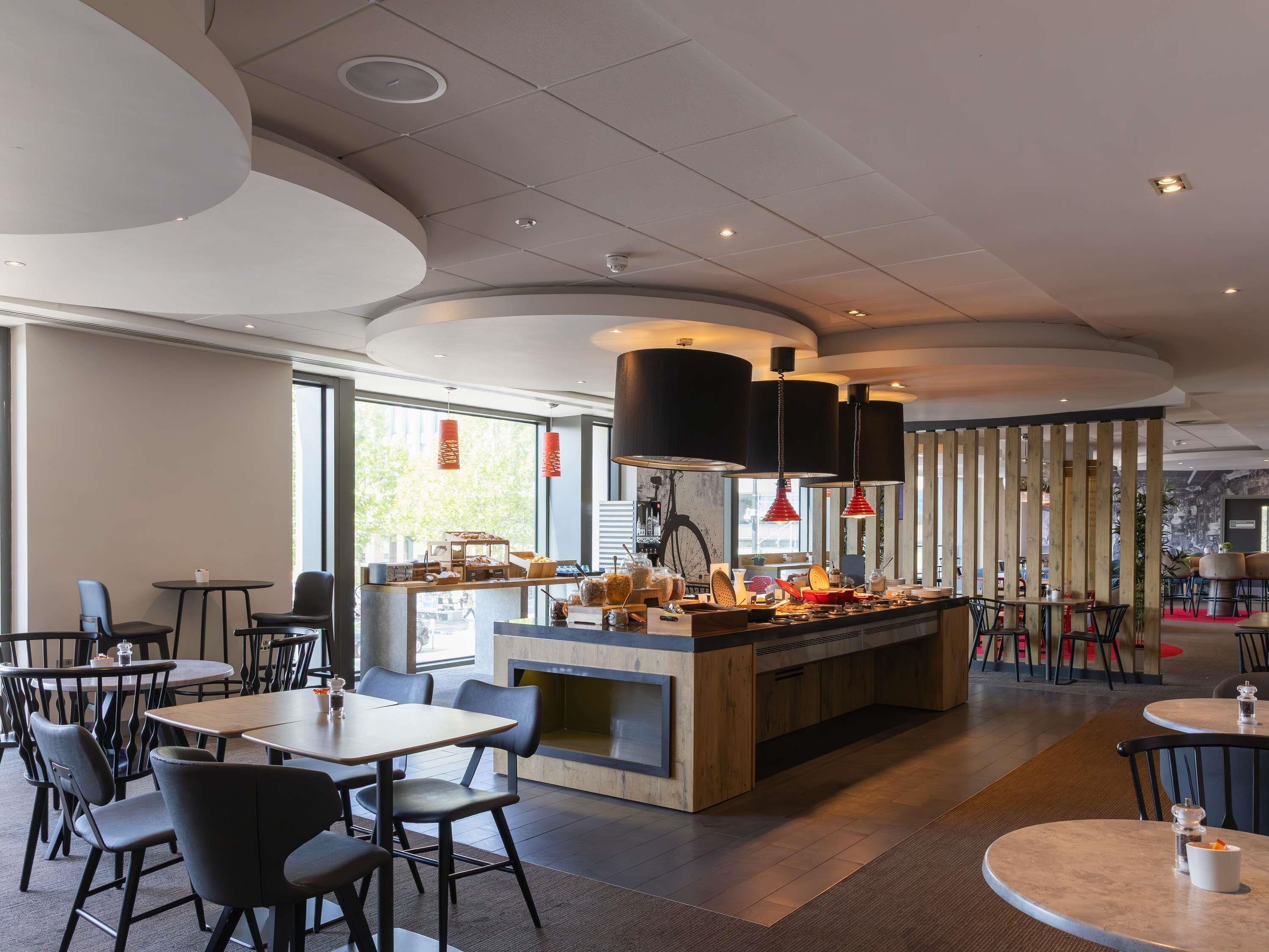 Un interior de restaurante moderno con una barra central, mesas redondas y sillas negras.
