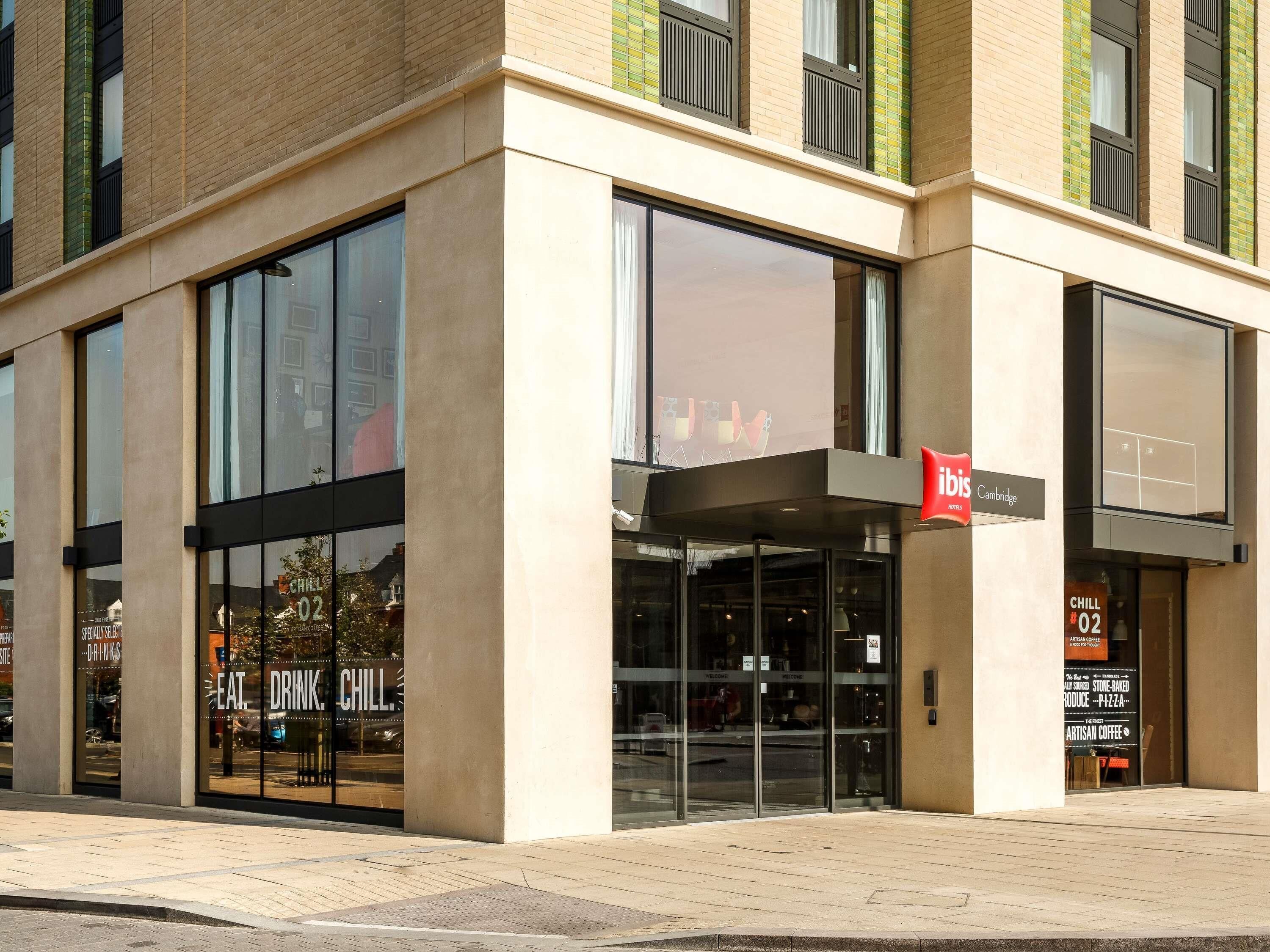 A modern building with large windows and a sign for 'ibis Cambridge'.