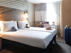 A hotel room with a bed, a desk, a suitcase, and a hat. - ibis Cambridge Central Station (Cambridge)