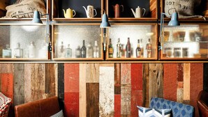 A bar area with shelves of bottles, a wooden wall with a patchwork design, leather chairs, and patterned cushions. - ibis Cambridge Central Station (Cambridge)