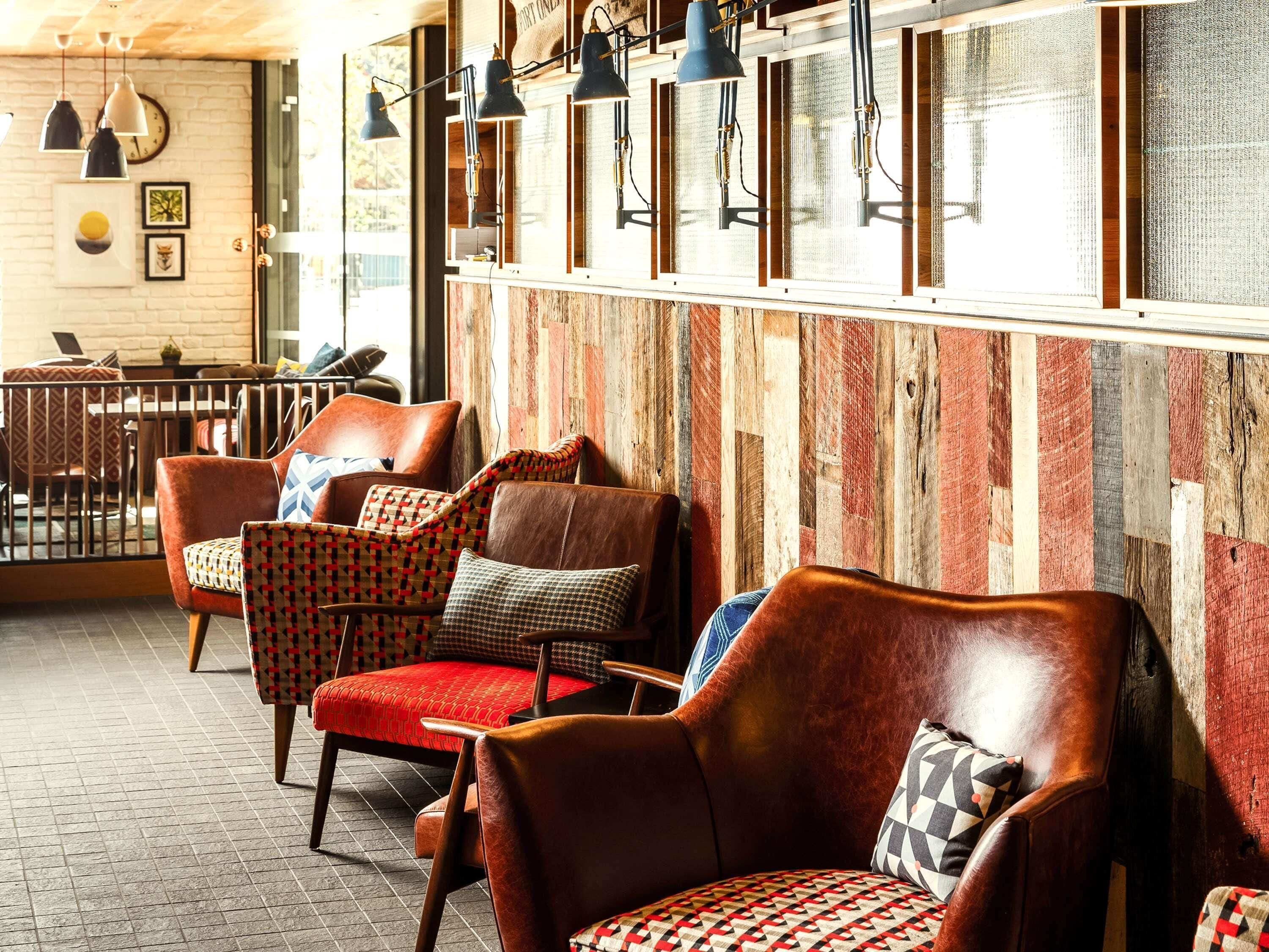 A cozy seating area with leather chairs and patterned cushions, wooden wall paneling, and pendant lighting.