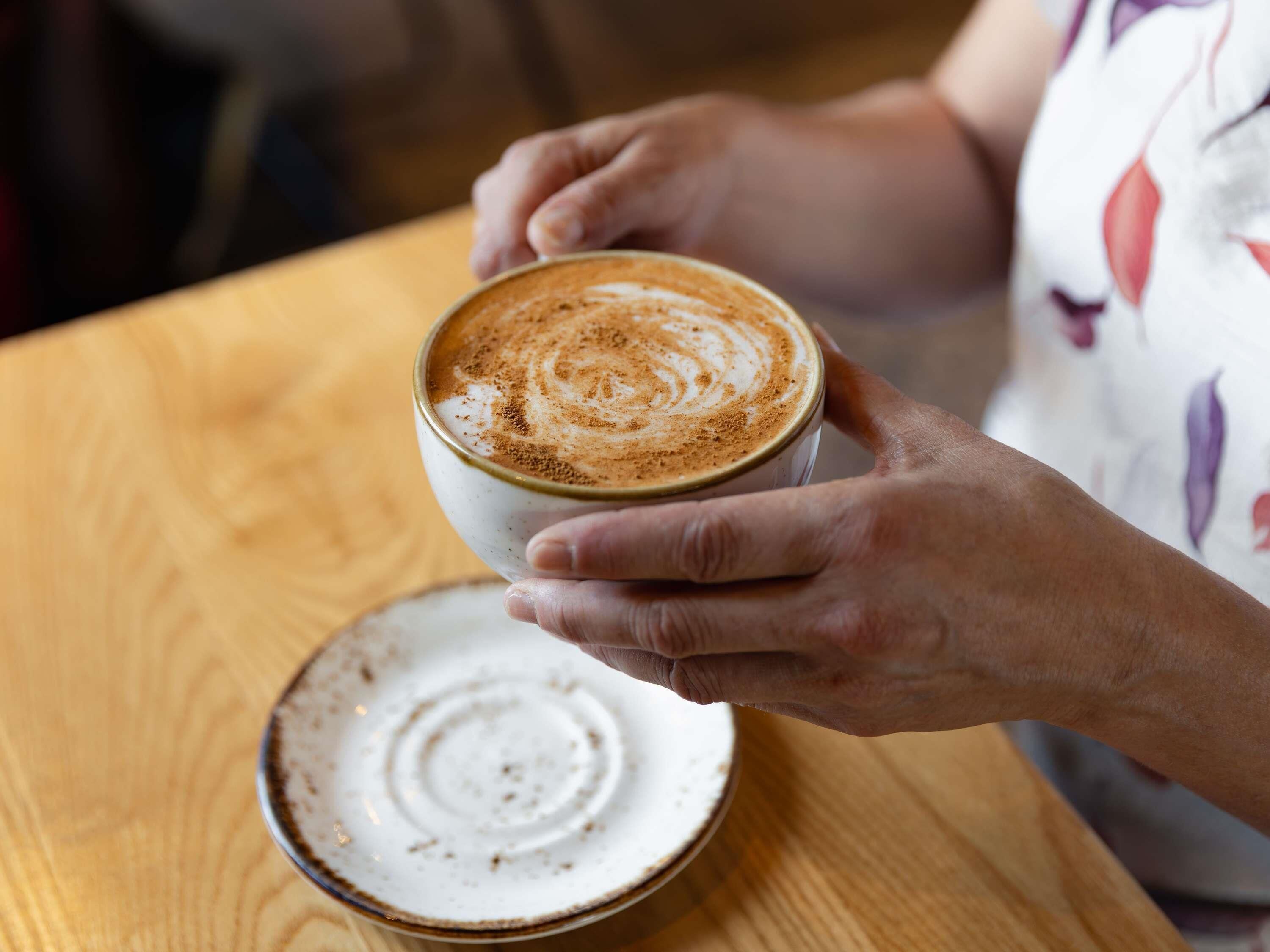 A person holding a cup of coffee with latte art on a wooden table.
