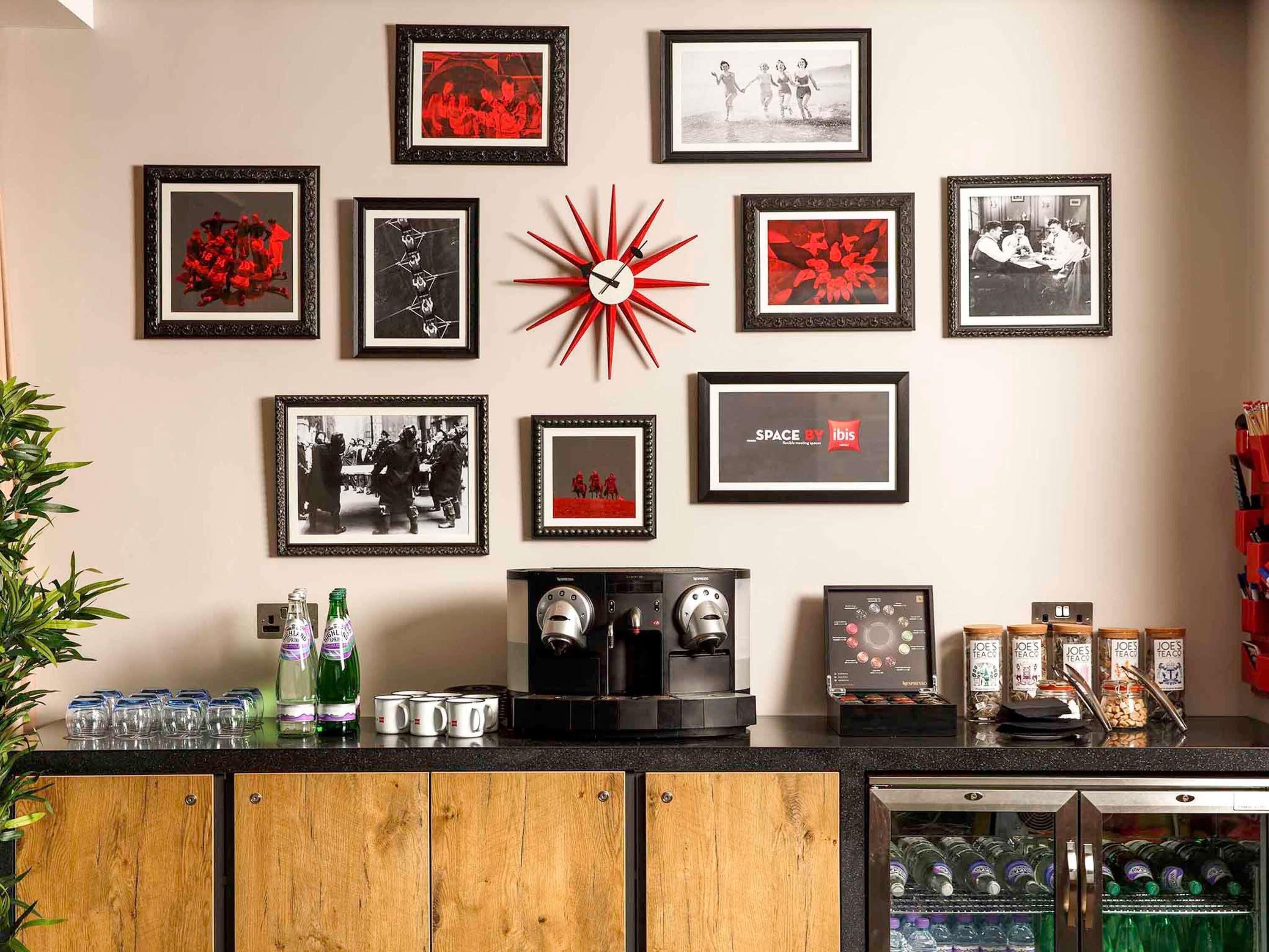 A kitchen with a coffee machine, a refrigerator, and various framed pictures on the wall.