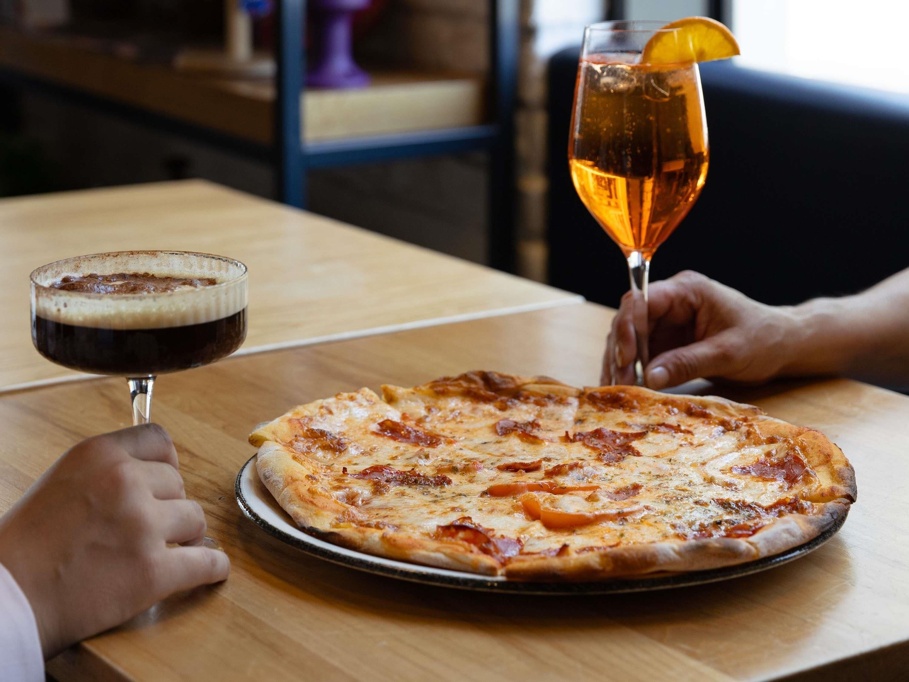 Una pizza sobre una mesa de madera, con una jarra de cerveza y un refresco.