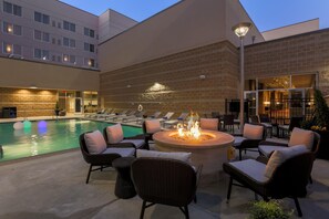 A poolside area with lounge chairs, a fire pit, and a building with a brick facade. - DoubleTree by Hilton Evansville (Evansville)