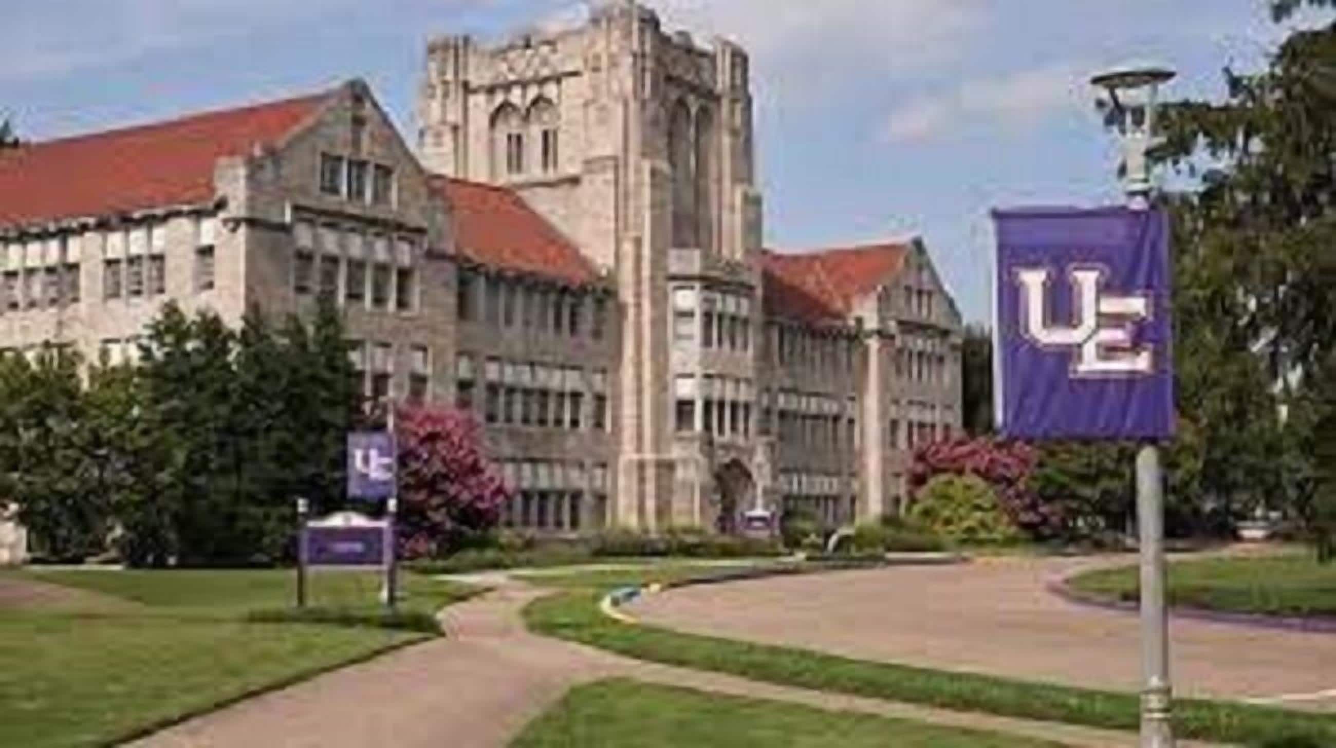 A large building with a prominent tower and a flag with a letter 'U' on a pole.